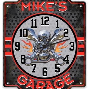 May include: A black and gray metal sign with a clock face featuring a skull and crossbones with flames. The clock face has the words "MIKE'S GARAGE" on it.