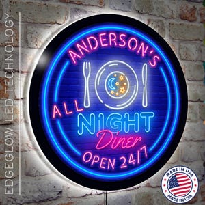 May include: A round neon sign with a blue background and pink and white neon lettering. The sign says "Anderson's All Night Diner Open 24/7". There is a white plate with a crescent moon and stars inside, and a fork and knife on either side of the plate.