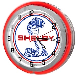 May include: Round wall clock with a red neon light border. The clock face features the Shelby logo with a blue cobra and the word "SHELBY" in red. The clock has black hands and numerals.