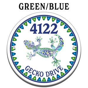 May include: Round white ceramic sign with a blue and green gecko design. The sign has a blue border with green and yellow accents. The number 4122 is printed in blue and the text "Gecko Drive" is printed in blue below the gecko.