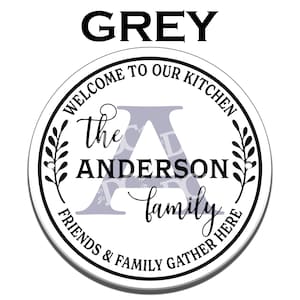 May include: A round, white sign with black text that reads "Welcome to our kitchen, the Anderson family, friends & family gather here". The sign has a large, grey letter "A" in the center.