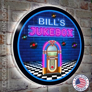 May include: A round, neon sign with a blue background and a black border. The sign features a vintage jukebox with a pink and blue neon sign that reads "BILL'S JUKEBOX". There are four black vinyl records hanging from the ceiling. The sign is made in the USA.