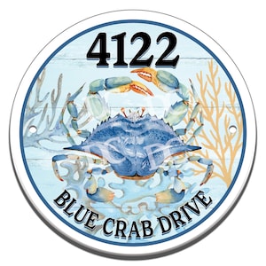 Könnte beinhalten: Ein rundes blaues und weißes Schild mit einem blauen Krebs auf einem blauen und weißen Holzgrund. Das Schild zeigt "4122 Blue Crab Drive".