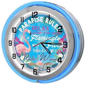 May include: A blue neon clock with a white face and a flamingo design. The clock face features the text "Paradise Rulez" and "Relax under the palm, Flamingle with the Flock, Get your feet wet, Ride the Wave, Watch the Sunset".