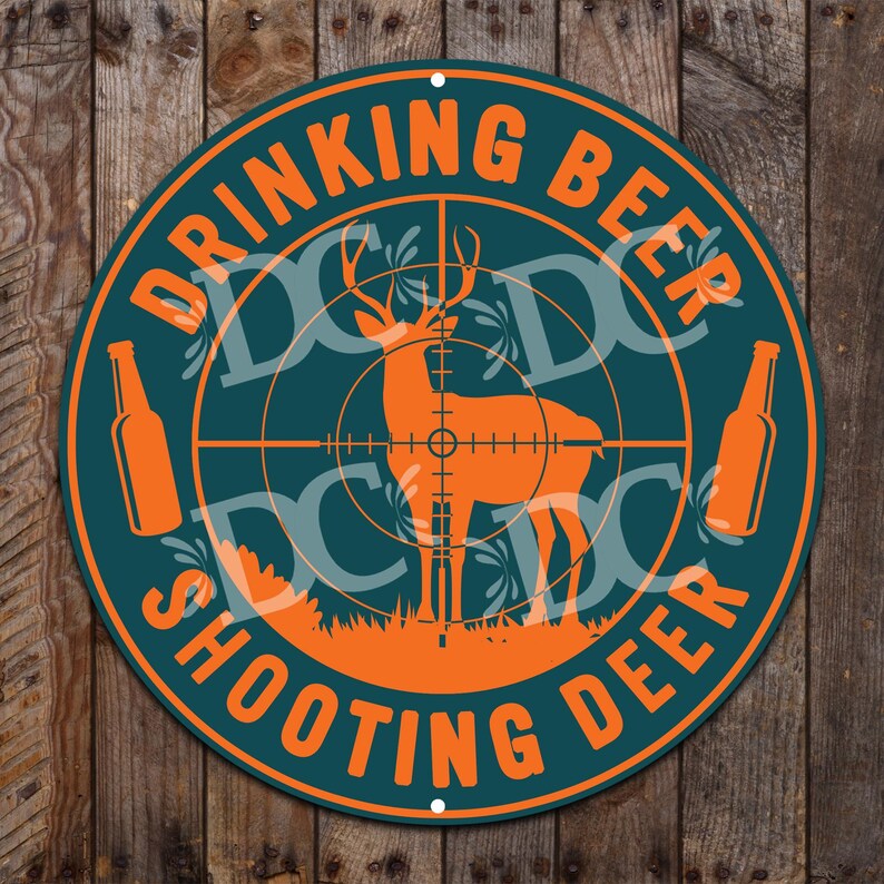 May include: A round, teal-colored metal sign with the text "Drinking Beer Shooting Deer" in orange letters. The sign features a deer silhouette in the center of a target with two orange beer bottles on either side.