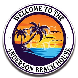 Könnte beinhalten: Rundes weißes Schild mit einer blauen, orangen und gelben Sonnenuntergangsszene mit Palmen. Der Text "Welcome to the Anderson Beach House" ist in einem schwarzen Kreis um die Sonnenuntergangsszene geschrieben.