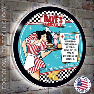 May include: A round, black-framed sign with a red, white, and blue diner theme. The sign features a cartoon waitress holding a tray with a hamburger and a milkshake. The text "Dave's Diner" is in a red and white font. The menu lists prices for various diner items, including hamburgers, cheeseburgers, hot dogs, french fries, soda, root beer floats, and sundaes. The sign also includes the text "Breakfast, Lunch & Dinner" and "Open 24/7".