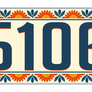Puede incluir: Una placa rectangular de número de casa con los dígitos 5106 en azul oscuro con contornos naranjas. La placa tiene un fondo color crema y un borde decorativo de pétalos de flores naranjas y hojas azul oscuro en los cuatro lados.