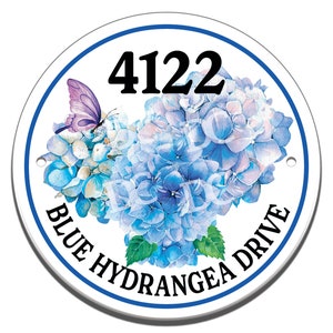 May include: Round white sign with a blue border, featuring a watercolor illustration of blue hydrangeas and a purple butterfly. The sign also includes the address number "4122" and the text "Blue Hydrangea Drive".
