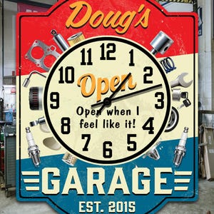 Peut inclure: Une horloge de style vintage avec une bordure rouge et bleue, affichant le texte "Doug's Garage" et "EST. 2015." Le cadran de l'horloge présente des pièces automobiles et les mots "Open when I feel like it!"
