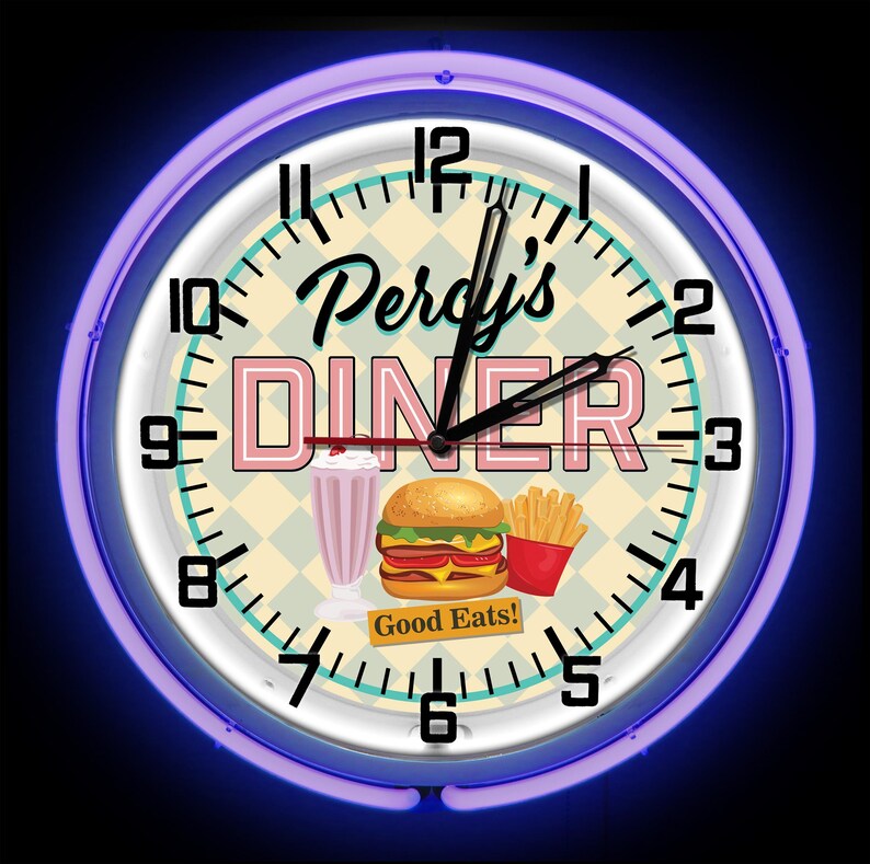 May include: Circular wall clock with a neon blue surround. The clock face displays "Percy's DINER" in pink and black, with illustrations of a milkshake, burger, and fries. The words "Good Eats!" are also visible.