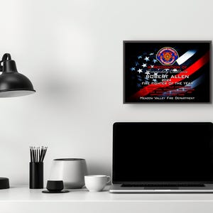 K&ouml;nnte beinhalten: Eine gerahmte Auszeichnung f&uuml;r Robert Allen, Feuerwehrmann des Jahres 2024, von der Meadow Valley Fire Department. Die Auszeichnung zeigt ein Design mit der amerikanischen Flagge, einem roten Streifen und dem Emblem der Feuerwehr.