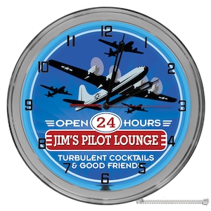 May include: A blue and silver neon clock with a vintage airplane design. The clock face reads "Open 24 Hours" and "Jim's Pilot Lounge". The text below reads "Turbulent Cocktails & Good Friends".