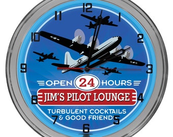 May include: A blue and silver neon clock with a vintage aeroplane design. The clock face reads "Open 24 Hours" and "Jim's Pilot Lounge". The text below reads "Turbulent Cocktails & Good Friends".