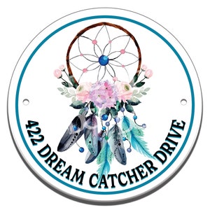 May include: A round white sign with a blue border and the text "422 Dream Catcher Drive" in black. The sign features a watercolor illustration of a dream catcher with feathers and flowers.