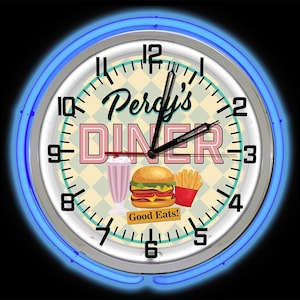 May include: Circular wall clock with a retro diner design. The clock face displays the text "Percy's DINER" in pink and black, alongside illustrations of a milkshake, burger, and fries. A blue neon light encircles the clock.