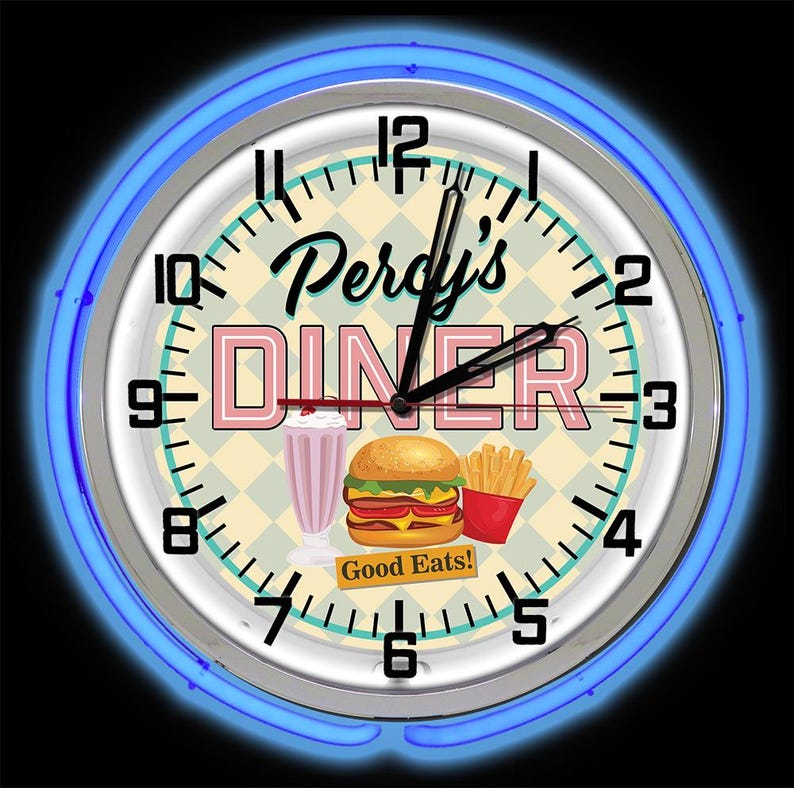 May include: Circular wall clock with a retro diner design. The clock face displays the text "Percy's DINER" in pink and black, alongside illustrations of a milkshake, burger, and fries. A blue neon light encircles the clock.