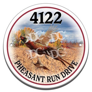 May include: A white round sign with a red border. The sign features a pheasant in flight over a field of golden wheat. The number 4122 is printed in black at the top of the sign. The words "Pheasant Run Drive" are printed in black around the bottom of the sign.