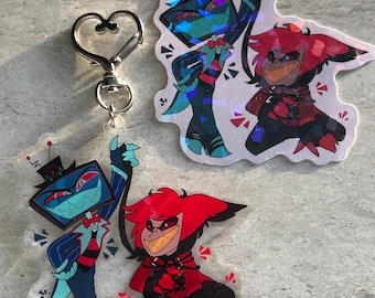 May include: A collection of character-themed merchandise, including a heart-shaped keychain and two clear acrylic charms. The charms feature colorful illustrations of animated characters in dynamic poses. One sticker with a holographic effect is also included.