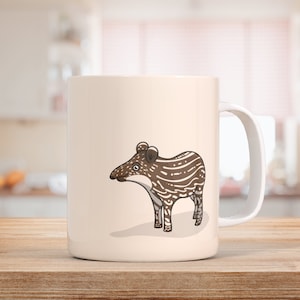 Könnte beinhalten: Eine weiße Keramiktasse mit einer braunen und weißen Cartoon-Tapir-Illustration. Der Tapir steht auf allen vieren und hat eine lange Schnauze.