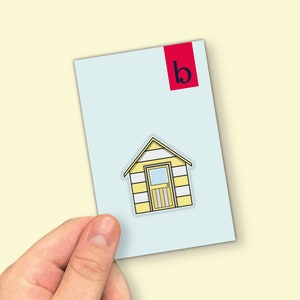 May include: A light blue card with a yellow and white striped beach hut illustration and the letter "b" in a red rectangle in the top right corner.