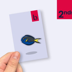 May include: A blue and black cartoon fish sticker with a yellow tail fin. The sticker is on a light purple background.