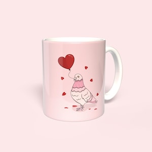May include: A pink and white ceramic mug with a cartoon illustration of a dove holding a red heart-shaped balloon. The mug is surrounded by small red hearts.