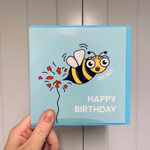 May include: A blue birthday card with a cartoon bee flying away from a red flower with the text "Oh no!" and "Happy Birthday".