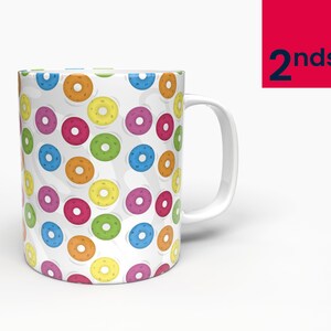 May include: White ceramic mug featuring a colourful donut pattern. The donuts are in various colours, including red, yellow, green, blue, and orange.