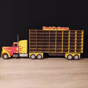 May include: A yellow and red toy semi-truck with a trailer that has a wooden shelf unit. The trailer has a sign that says "Daniel's Garage".