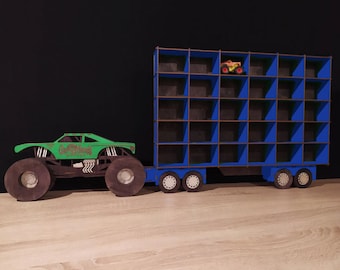 May include: A green monster truck with the words "Grave Digger" on the side is pulling a blue wooden toy trailer with 24 compartments. The trailer has a small toy monster truck in one of the compartments.
