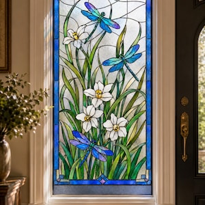 May include: A rectangular stained glass window panel featuring three vibrant blue and purple dragonflies hovering over white daffodils with yellow centers. The design includes long green leaves and a clear textured glass background with a blue border.