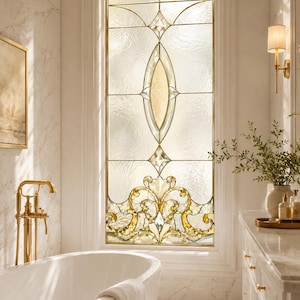 May include: A rectangular stained glass window featuring a central vertical oval motif and intricate gold-toned scrollwork at the base. The glass panels have a textured, translucent finish framed by thin metal cames, set within a white wall.