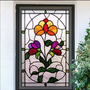Può includere: Una vetrata con un disegno floreale. I fiori sono arancioni, gialli, rossi e viola, con foglie verdi, su uno sfondo bianco strutturato. La finestra è incorniciata in nero.
