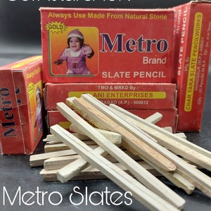 May include: A pile of white slate pencils, with a red box labeled "Metro Brand Slate Pencil" in the background. The box has a gold sticker that says "Gold" and a picture of a child. The box also says "Always Use Made From Natural Stone".