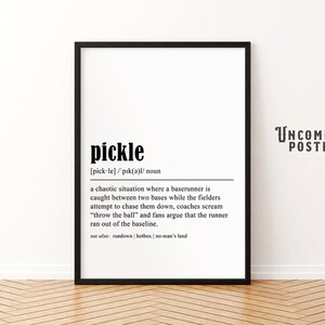 May include: A framed black and white print with the definition of the word "pickle" from the Uncommon Poster Co. The definition describes a chaotic baseball situation. The print is displayed on a white wall.