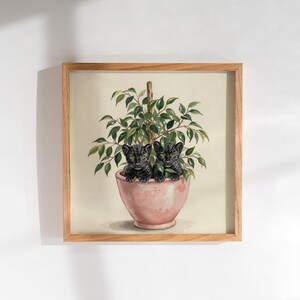 Op de afbeelding: Een vierkante ingelijste kunstdruk met een aquarelillustratie van twee kleine zwarte panterwelpen die in een lichtroze keramische plantenpot zitten. Een groene bladplant groeit uit de pot, ondersteund door een dunne houten stok in het midden.