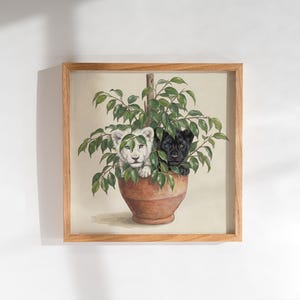 May include: A square framed wall art print featuring a painting of a white lion cub and a black panther cub peeking out from behind the green leaves of a potted plant. The plant is housed in a terracotta-colored pot, set against a light background.