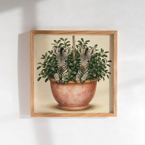 Peut inclure: Une impression d'art murale carrée encadrée représentant deux zébreaux émergeant d'une plante aux feuilles vertes denses dans un pot arrondi de couleur terre cuite. L'œuvre est sur fond crème clair dans un cadre en bois clair.