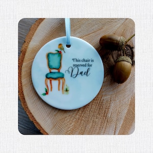 May include: White ceramic ornament with a blue chair and a bird on a branch. The ornament has the text "This chair is reserved for Dad" on it.