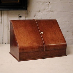 Può includere: Una scatola di legno per scrivere con un coperchio incernierato e un buco della serratura. La scatola è chiusa e ha una finitura marrone scuro.