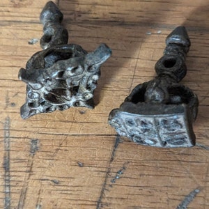 May include: Two antique silver-toned metal decorative pieces with intricate designs. The pieces are shaped like small towers with pointed tops and detailed carvings.