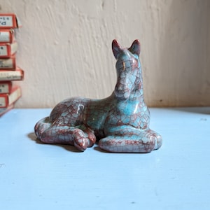 May include: A ceramic figurine of a horse in a light blue and red crackle glaze. The horse is lying down with its head turned to the side.