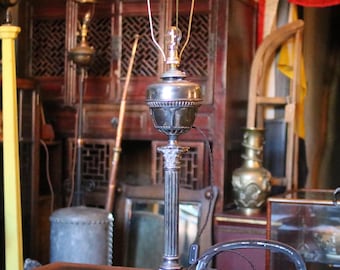 May include: A silver table lamp with a column-shaped base and a round shade. The lamp has a simple design and is in good condition.