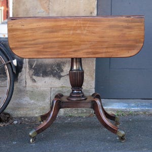 May include: A mahogany drop leaf table with a turned pedestal base and four cabriole legs with brass castors. The table is in a traditional style and has a rich brown finish.
