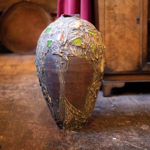 Könnte beinhalten: Eine braune Keramikvase mit strukturierter Oberfläche und grünen Glasakzenten. Die Vase hat ein einzigartiges, organisches Design.