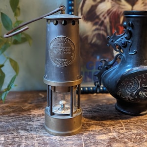 Könnte beinhalten: Eine Messing-Bergmannslampe mit einer klaren Glasschutzhaube und einem Metallgriff. Die Lampe trägt ein Etikett mit der Aufschrift "Inspector Lamp & Lighting Type 6 Ministry of Power Safety Lamps Approval Piece Makers Goole's".