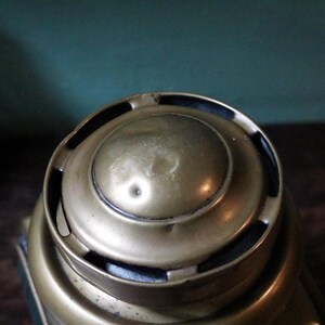 May include: Close-up of a vintage brass object with a rounded top and circular design. The brass has a warm, aged patina, with visible wear and slight dents. The object's design suggests it may be a decorative or functional item.