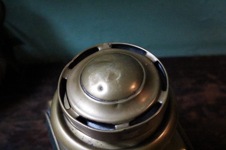 May include: Close-up of a vintage brass object with a rounded top and circular design. The brass has a warm, aged patina, with visible wear and slight dents. The object's design suggests it may be a decorative or functional item.