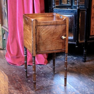 May include: A wooden bedside table with a single door and four legs. The table has a dark wood finish and a light wood top. The door has a brass handle.
